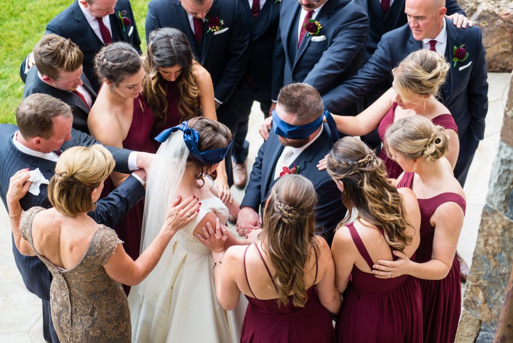 The couple meeting blindfolded as their friends and family surround them in a prayer circle.